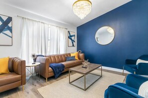 A living room with a brown sofa, blue armchair, and a coffee table. - 5BD Relaxing Stay- Game Room, Spa, Ping-Pong Table (North Las Vegas)