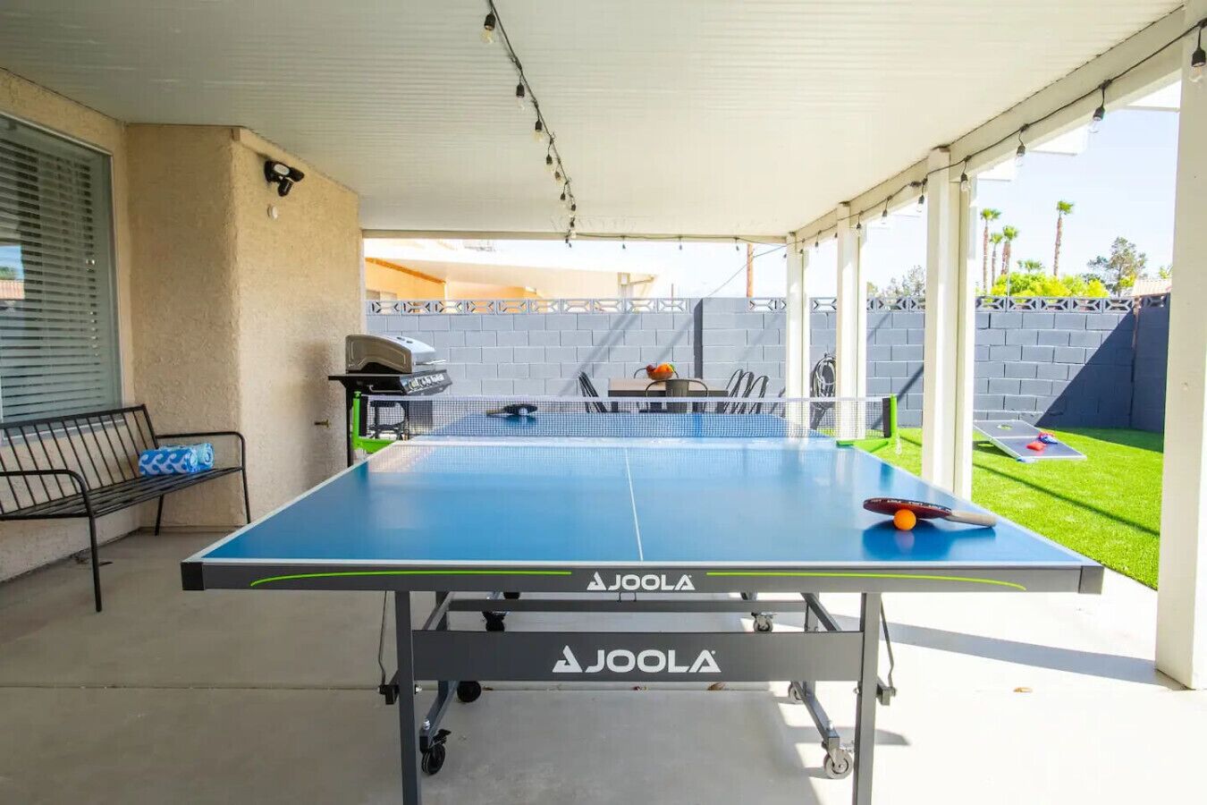 An outdoor table tennis table with a net, a grill, and a bench.