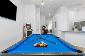 A pool table with balls, a pool cue, and two arcade machines in a room with white walls and a ceiling light. - 5BD Relaxing Stay- Game Room, Spa, Ping-Pong Table (North Las Vegas)