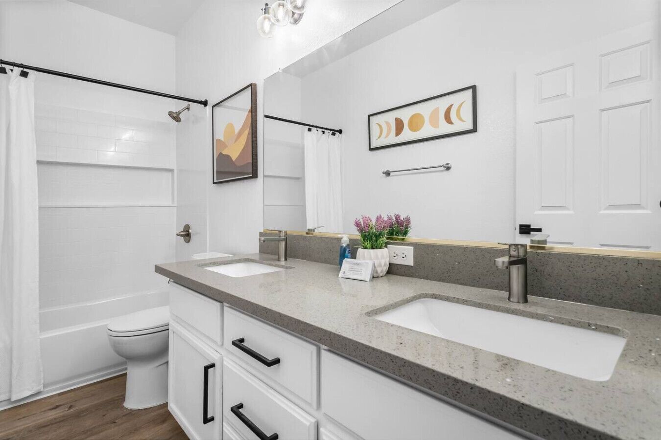 Un baño con dos lavamanos, inodoro, ducha y espejo con decoración artística.