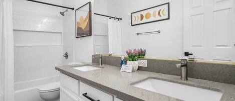 Un baño con dos lavamanos, inodoro, ducha y espejo con decoración artística.