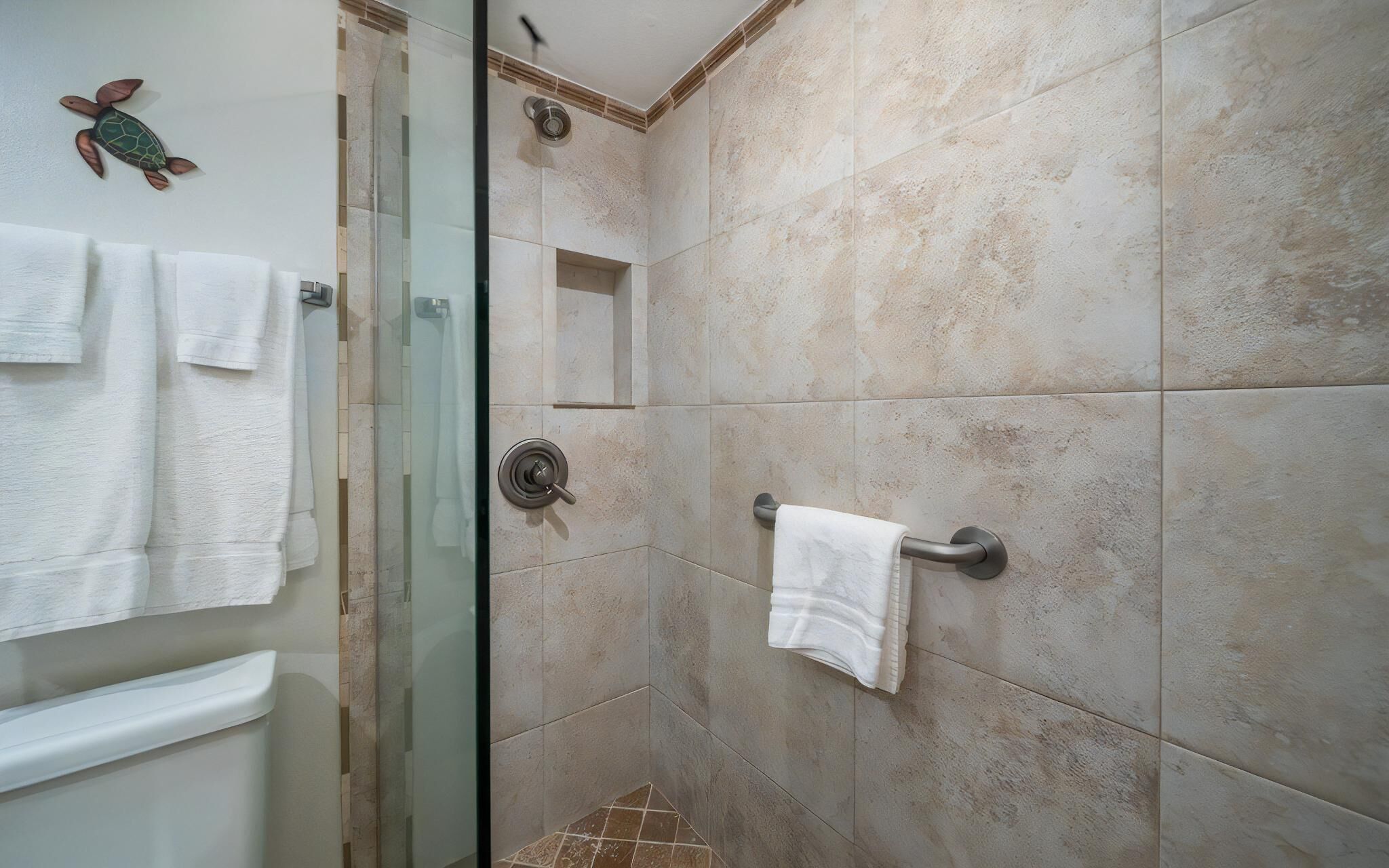 Casa de banho com cabine de duche em vidro, porta-toalhas e dispensador de toalhas fixado à parede.