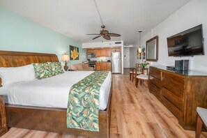 Habitación de hotel con cama, escritorio, silla, televisor y kitchenette.