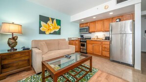 A living room with a sofa, coffee table, and a painting of a flower. - Royal Kahana Maui 719 Ocean View Studio (Lahaina)