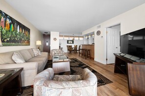 A living room with a sofa, armchair, coffee table, and a painting of surfboards.