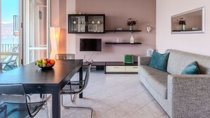 A modern living room with a dining area, a TV mounted on the wall, and a balcony with a view. - Apartment Lella by Interhome (Varenna)