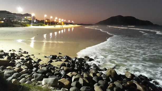 A beach with a rocky shoreline and a row of lights along the beach. - APARTMENT FREE FOR NEW YEAR'S EVE. (Ingleses Sul Florianópolis)