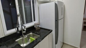 A kitchen with a stainless steel sink, a refrigerator, and a window with a view of the outdoors. - APARTMENT FREE FOR NEW YEAR'S EVE. (Ingleses Sul Florianópolis)