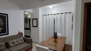 A dining area with a wooden table and chairs, a grey sofa, and a ceiling fan. - APARTMENT FREE FOR NEW YEAR'S EVE. (Ingleses Sul Florianópolis)