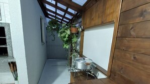 A narrow, enclosed patio with a wooden bench, a small table with a pot, and a potted plant. - APARTMENT FREE FOR NEW YEAR'S EVE. (Ingleses Sul Florianópolis)
