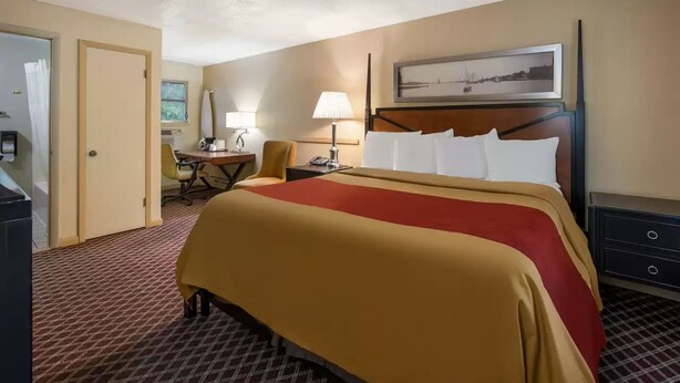 Een hotelkamer met een groot bed, een bureau, een stoel, een lamp en een schilderij aan de muur.