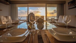 A dining table set for two with a view of the sunset over the ocean. - Exclusive Pent House, stunning ocean and lagoon views (Cancún)