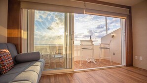 A modern living room with a sliding glass door leading to a balcony with a table and chairs. - Exclusive Pent House, stunning ocean and lagoon views (Cancún)