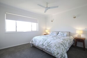 Un dormitorio con una cama, dos lámparas de noche, un ventilador de techo y una ventana.