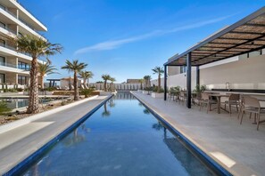 A swimming pool with lounge chairs and palm trees, surrounded by modern buildings with outdoor seating areas. - 2 Pools, Jacuzzi, Close to Beaches, Rooftop, Cozy (Cabo San Lucas)