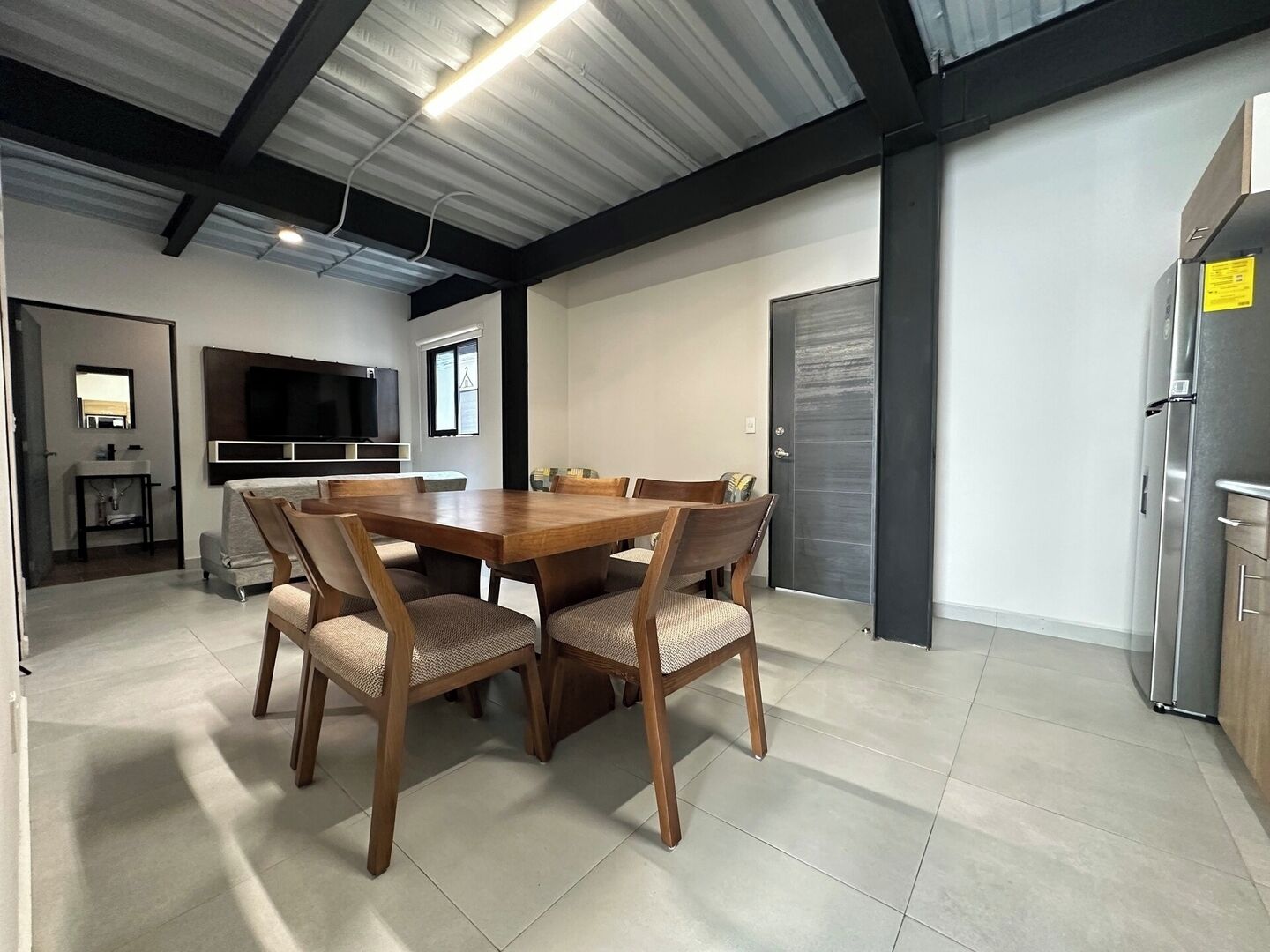 A modern kitchen with a dining area, featuring a large wooden table and chairs, a built-in oven, and a refrigerator.
