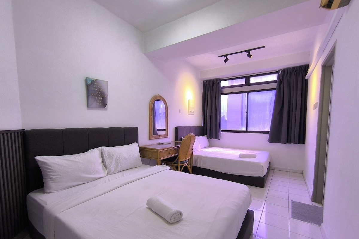 A hotel room with two beds, a desk, a chair, a window with curtains, and a wall-mounted mirror.