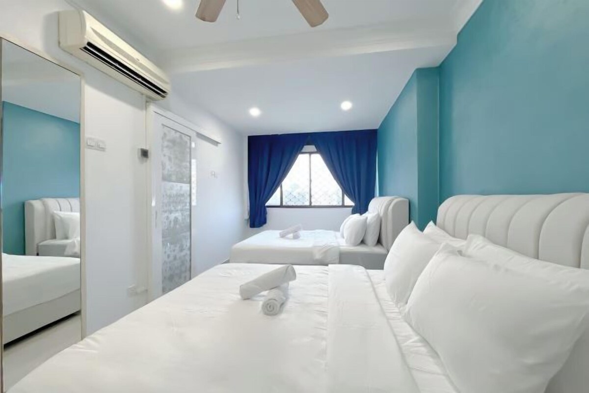 A hotel room with a large bed, a smaller bed, a bathroom with a mirror, and a window with blue curtains.