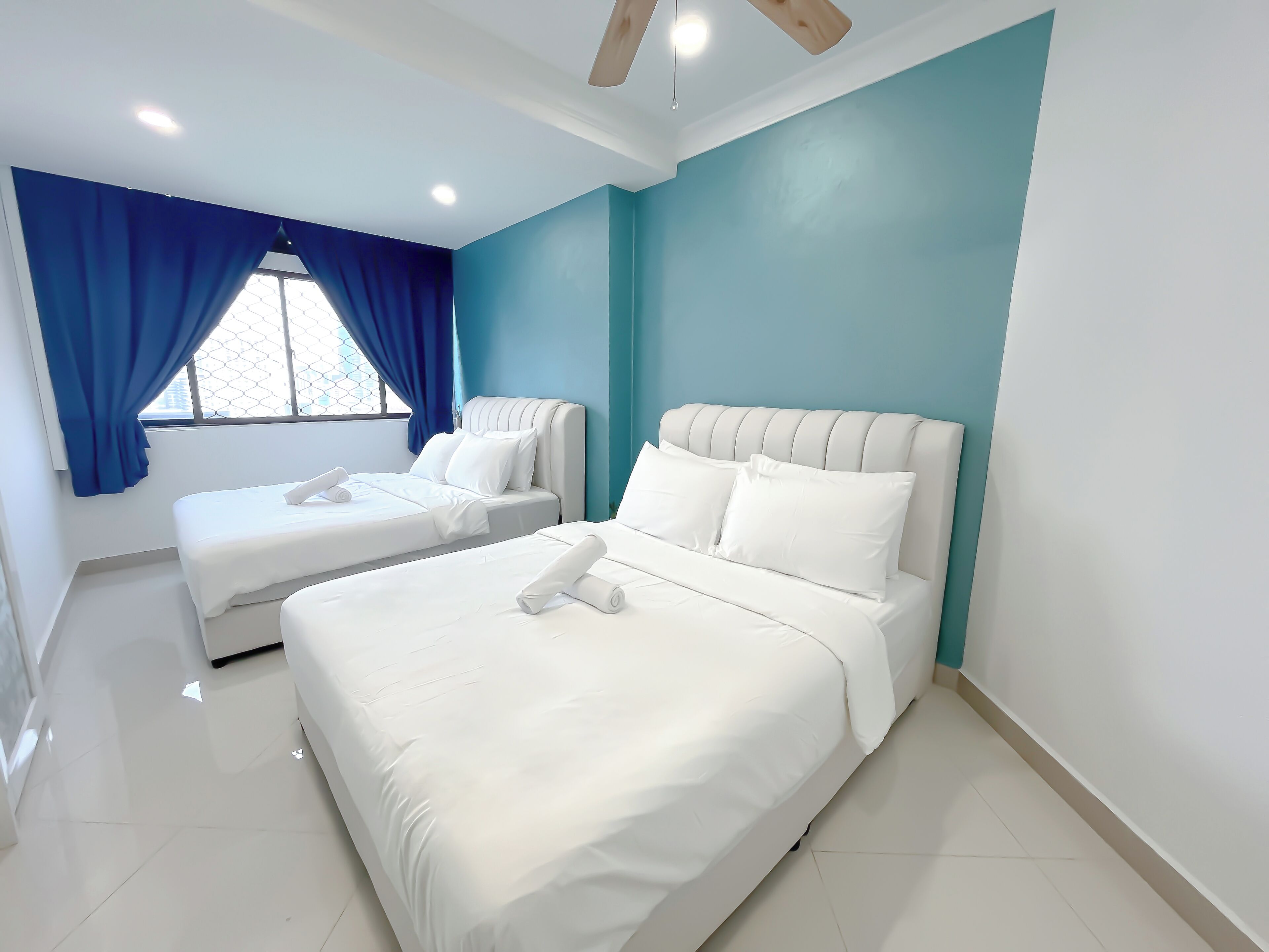 A hotel room with two beds, a window with blue curtains, and a ceiling fan.