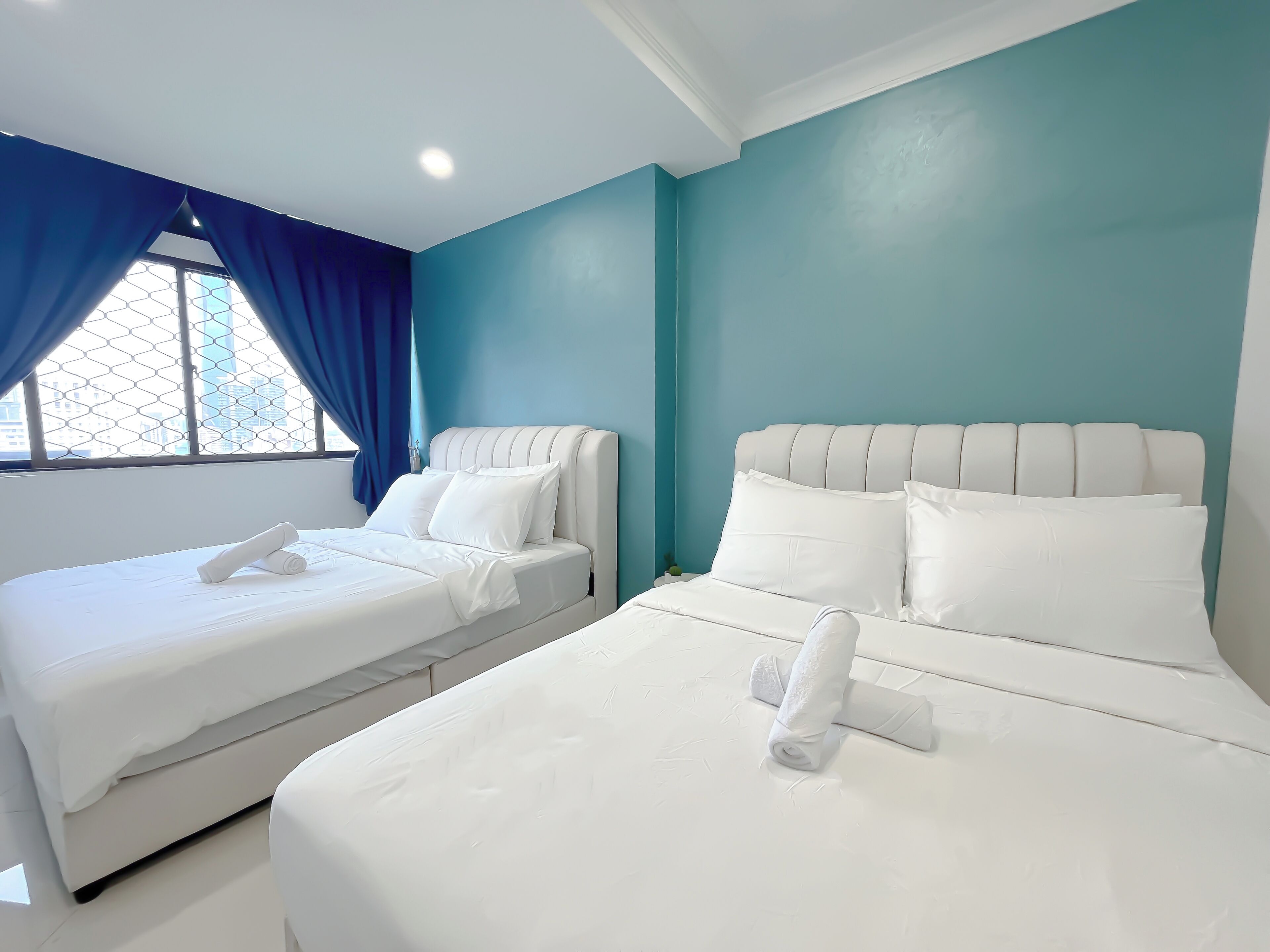 Een hotelkamer met twee bedden, elk voorzien van witte lakens en kussens, en een raam met blauwe gordijnen.