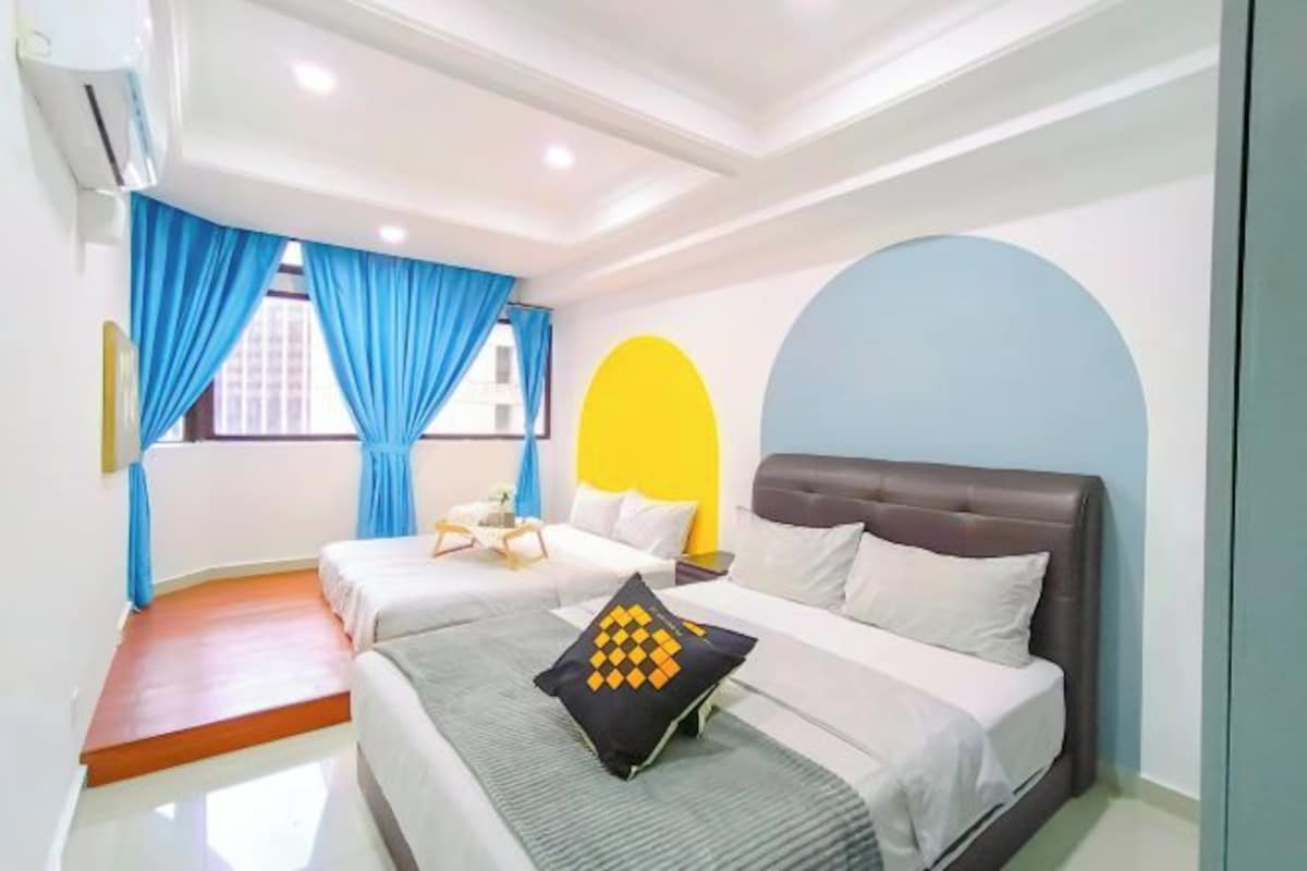 A hotel room with two beds, a large window with blue curtains, a ceiling fan, and a modern design with a yellow accent wall.