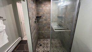 Une douche fermée par des parois de verre, avec un sol carrelé en pierre et un porte-serviettes blanc.