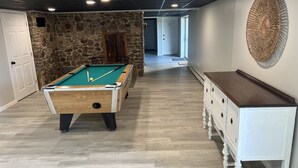Une table de billard dans une pièce avec un mur en pierre, un plancher en bois et une commode blanche.