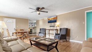 A living room with a sofa, a coffee table, and two chairs. There is a ceiling fan, a TV mounted on the wall, and a dining table with chairs. - Affordable, Private, Single Level House Steps From Hard Rock Casino Pet Friendly (Bristol)