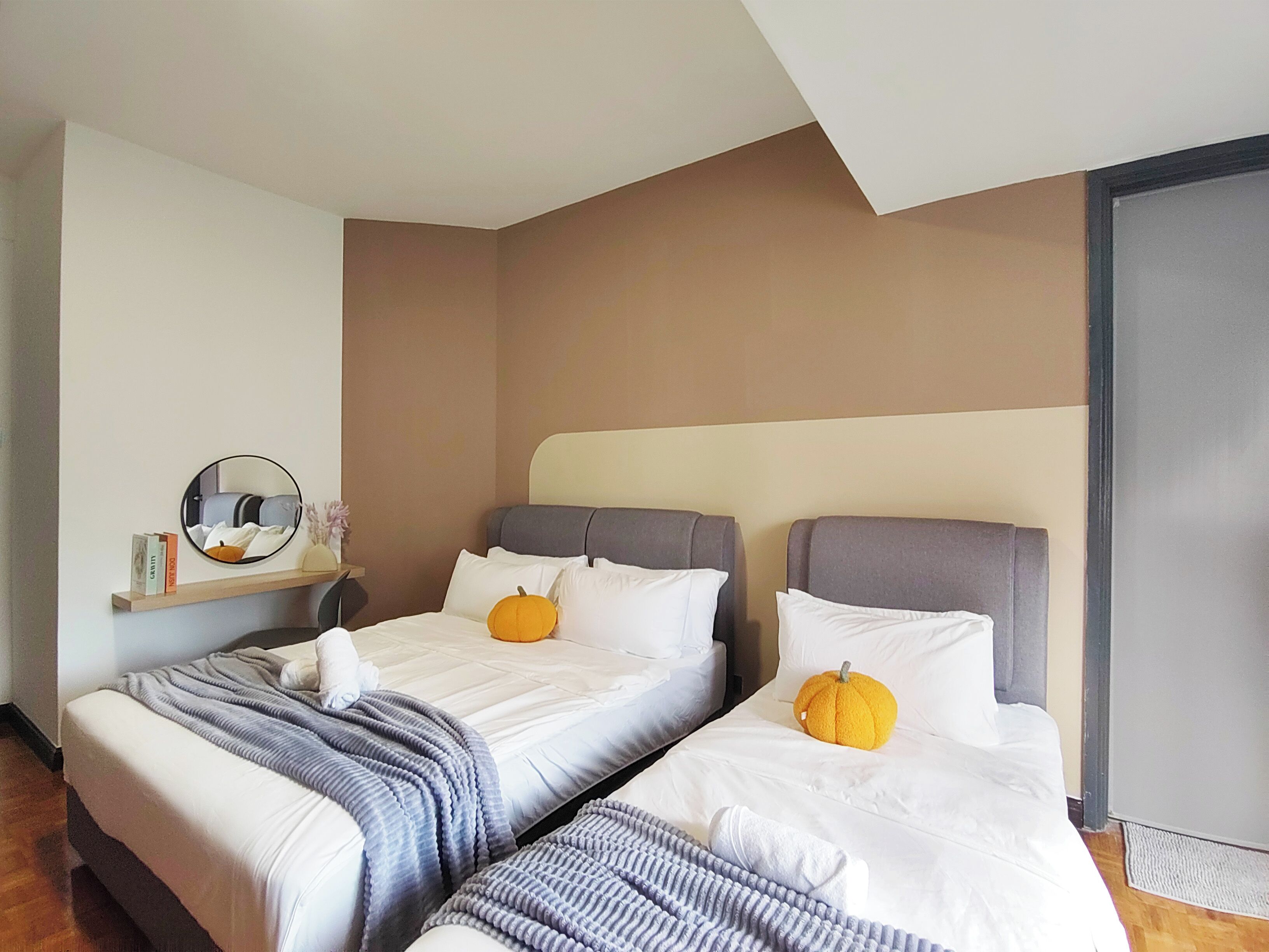 A hotel room with two beds, a mirror, and a shelf with books and a vase.