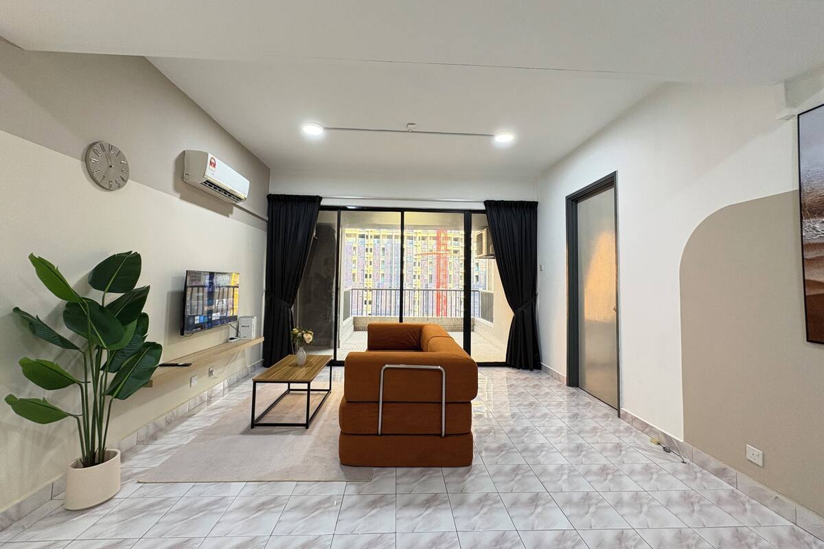 A modern living room with a sofa, a potted plant, a TV, and a balcony with a city view.