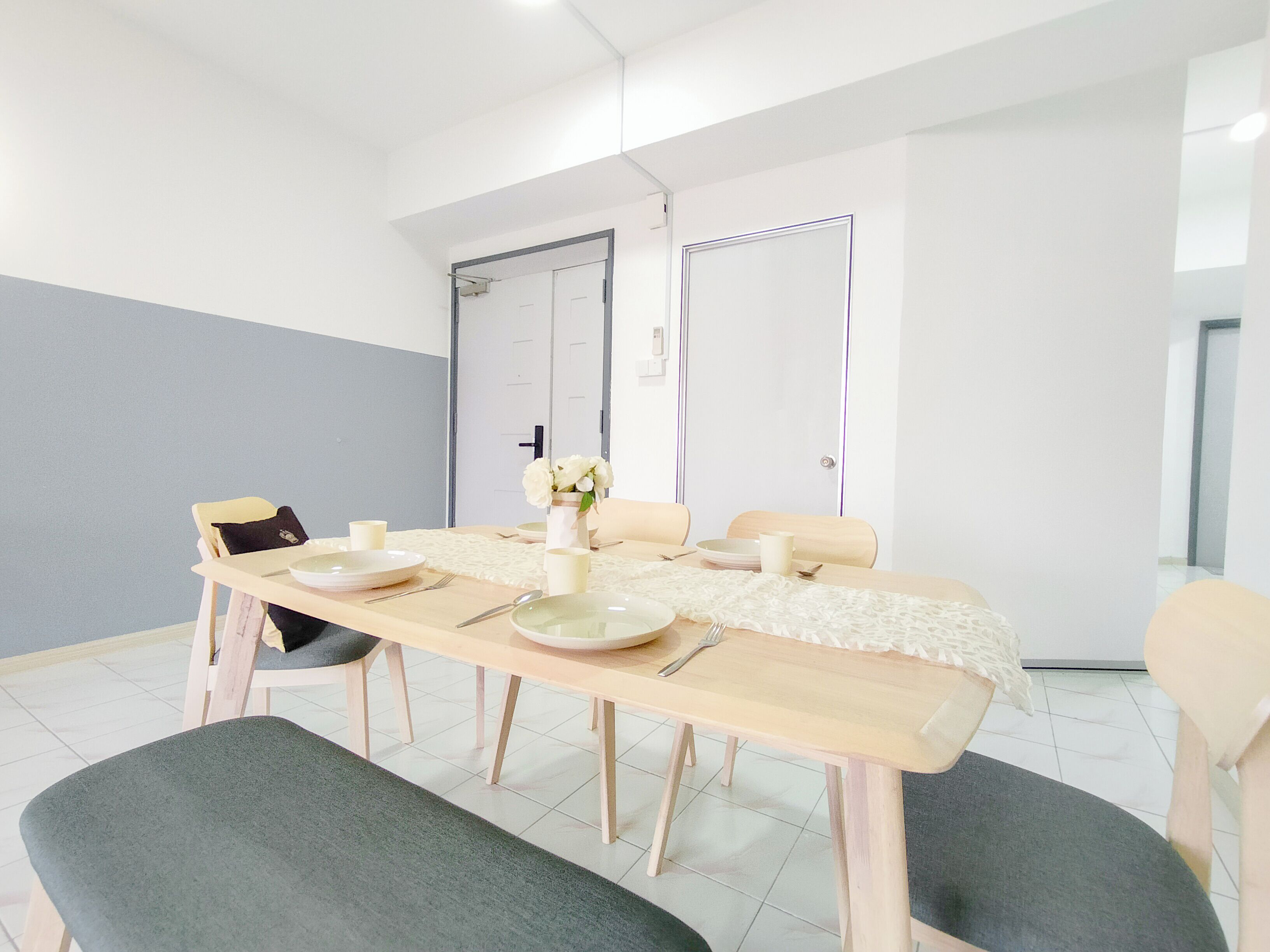 Un coin repas avec une table en bois dressée pour quatre personnes, des chaises et un vase de fleurs.