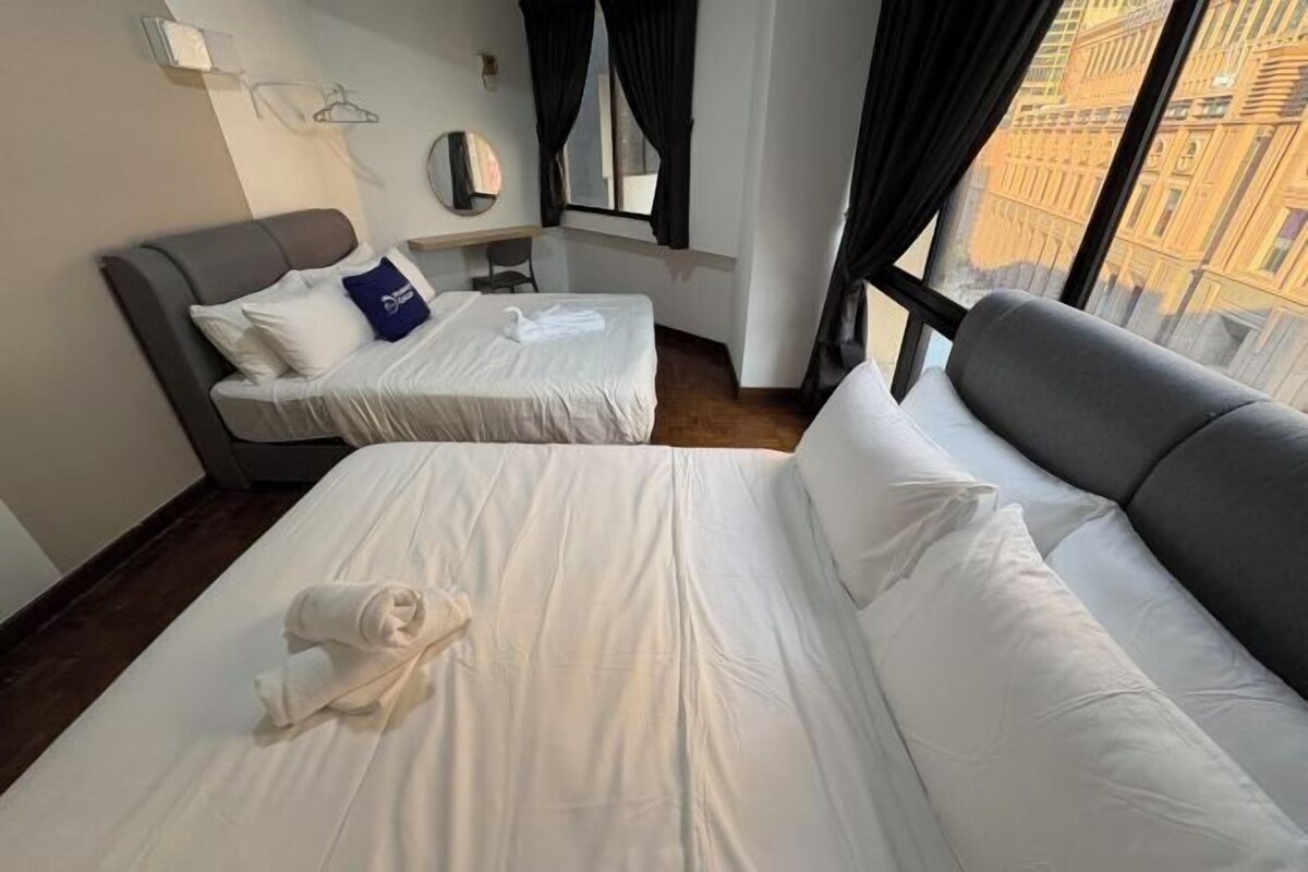 A hotel room with two beds, a desk, a chair, a mirror, and a window with a city view.