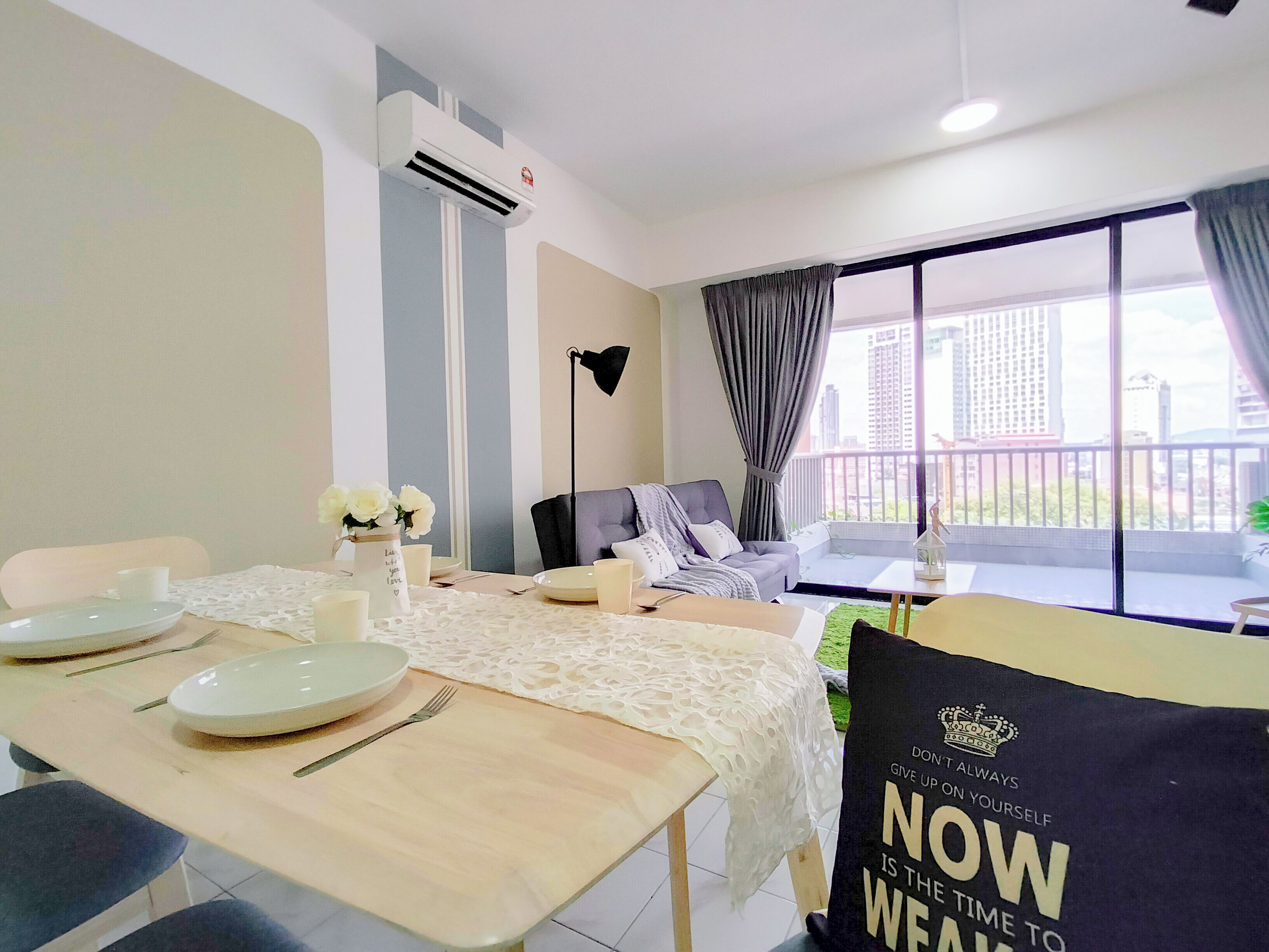 A modern living room with a dining area, a sofa, a table set for two, and a balcony with a view of the city.