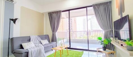 A modern living room with a grey sofa, a green rug, and a large window with curtains.