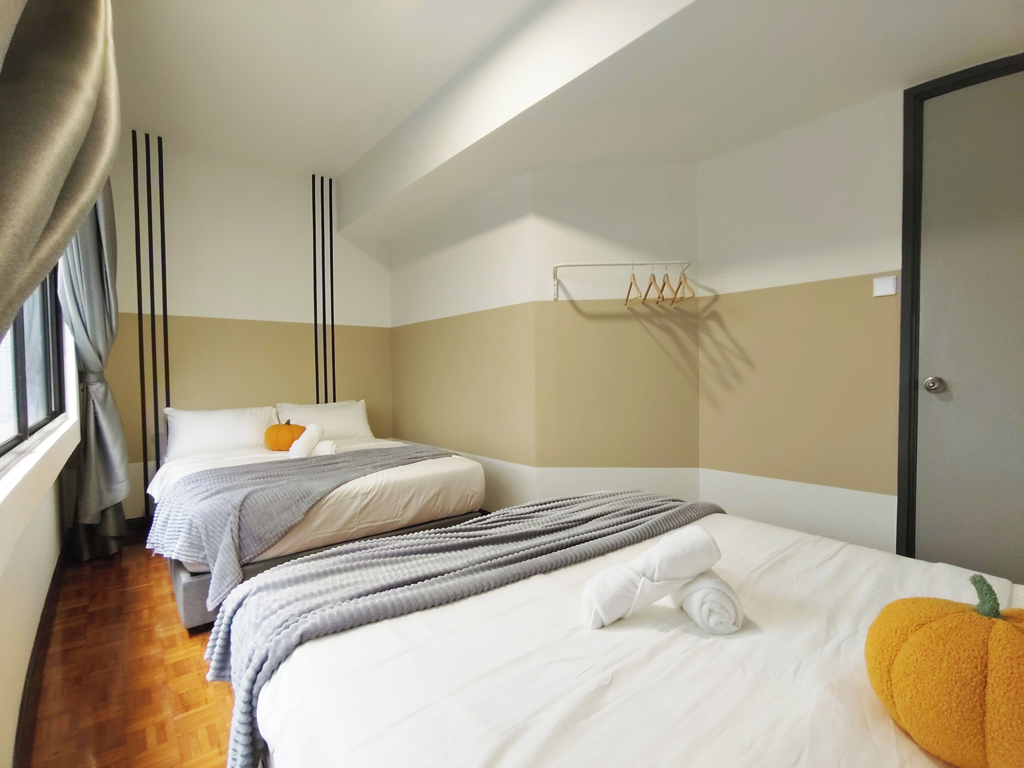 A hotel room with two beds, a window with curtains, a towel rack, and a door.