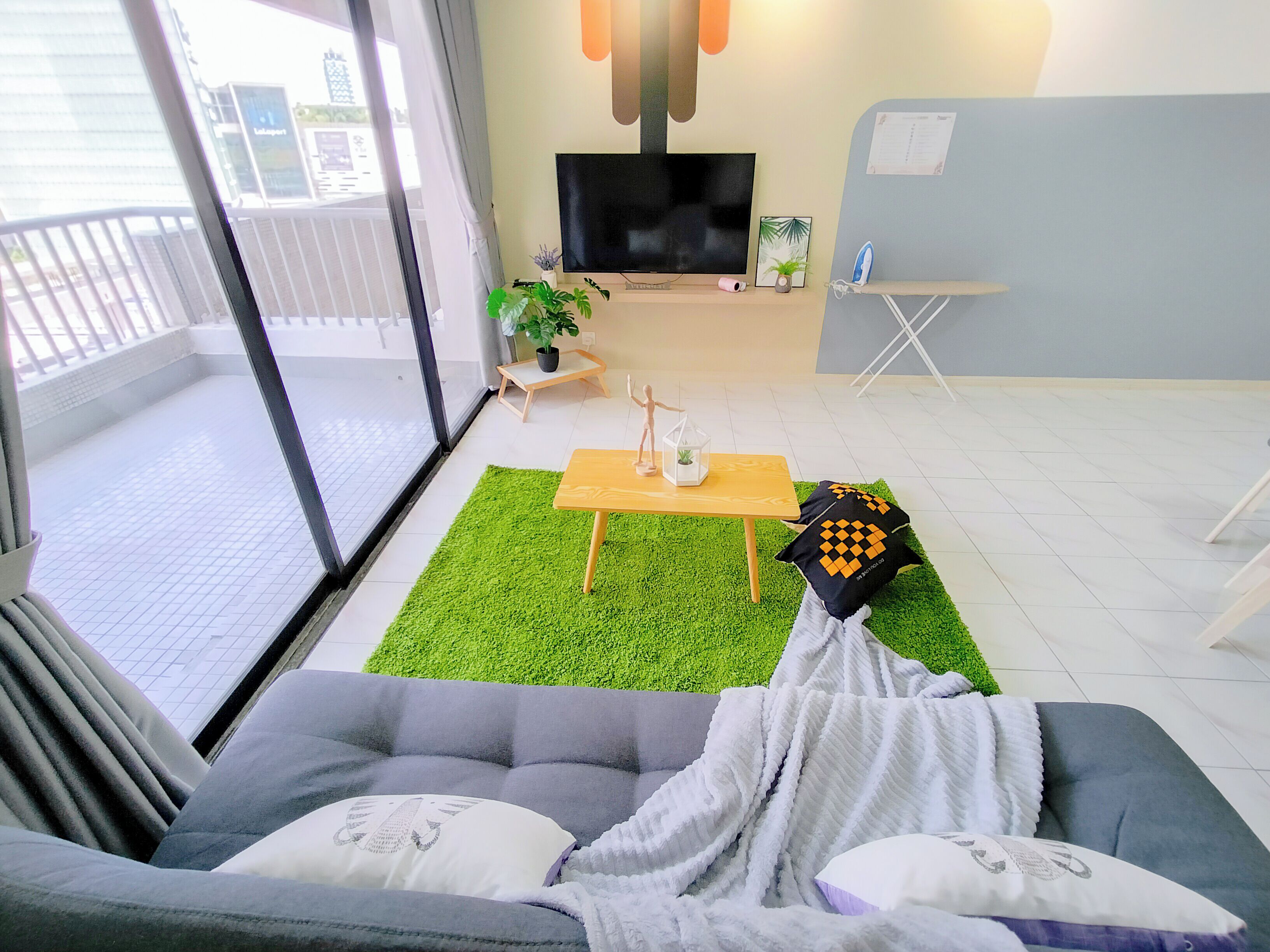 A modern living room with a grey sofa, a wooden coffee table, a green rug, and a flat-screen TV.