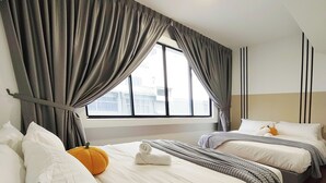 Habitación de hotel con dos camas, cortinas grises, una ventana con vistas a edificios y suelo de madera.