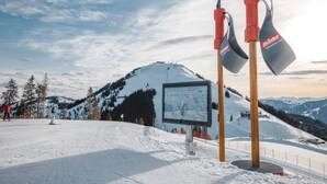 A ski resort with a snow-covered slope, a ski lift, and a signboard. - Cosy Apartment on the Ski-slope (Hopfgarten im Brixental)