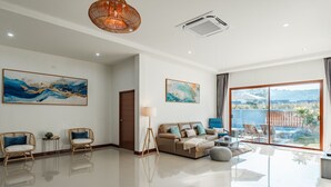 A spacious living room with a large window, a sofa, two armchairs, and a floor lamp.