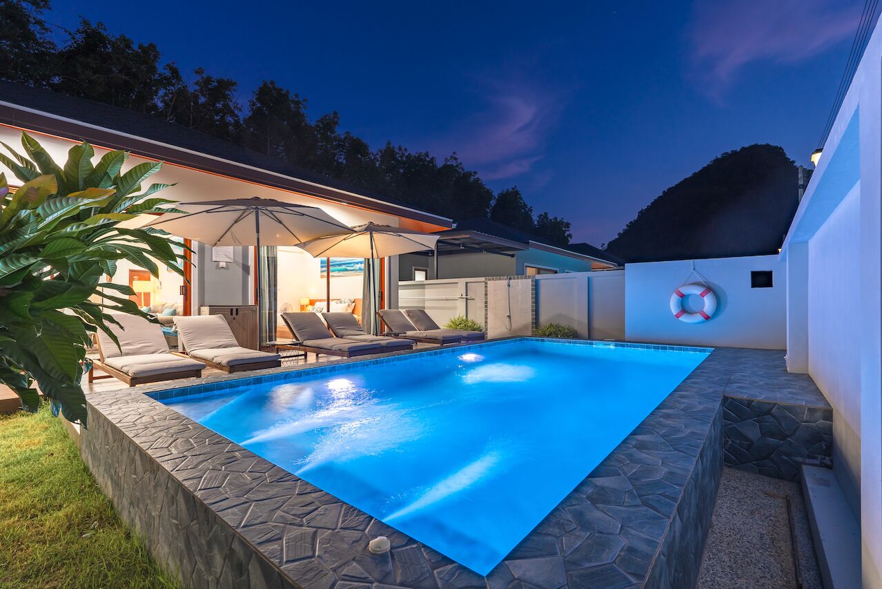 Une piscine entourée de chaises longues et de parasols, le tout bordé de murs en pierre et d’une pelouse.