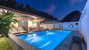 A swimming pool with lounge chairs and umbrellas, surrounded by stone walls and a grassy area.
