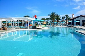 Ein Swimmingpool mit Liegestühlen und Sonnenschirmen, umgeben von Palmen und einem überdachten Bereich mit einem roten Sessel.