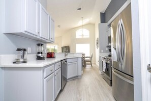 A modern kitchen with white cabinetry, stainless steel appliances, and a light wood floor.
