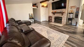 A living room with a sectional sofa, a fireplace, a television, and a ceiling fan.