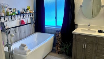 A modern bathroom with a bathtub, a vanity with a mirror, and a window with curtains.