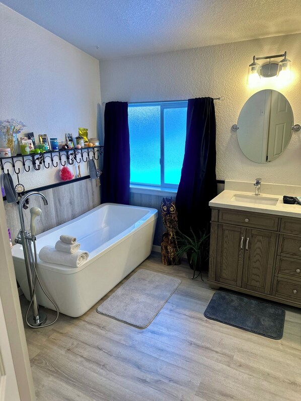 Ein modernes Badezimmer mit einer Badewanne, einem Waschtisch mit Spiegel und einem Fenster mit Vorhängen.
