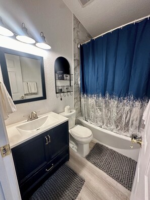 Ein modernes Badezimmer mit Waschbecken in Weiß, einem schwarzen Waschtisch, einer Toilette und einer Badewanne mit blauer Duschvorhang.
