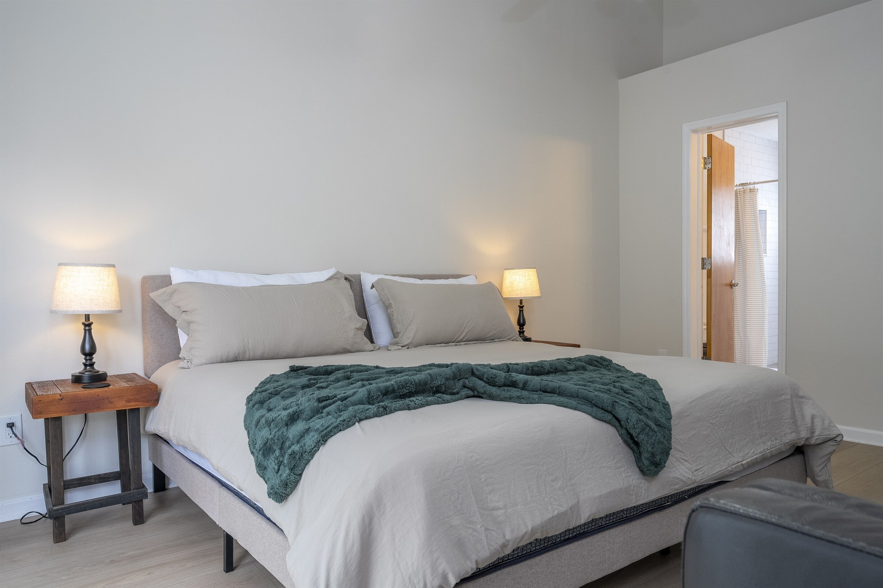 Ein ordentlich gemachtes Bett mit grüner Decke, zwei Nachttischlampen und einem Nachttisch aus Holz.