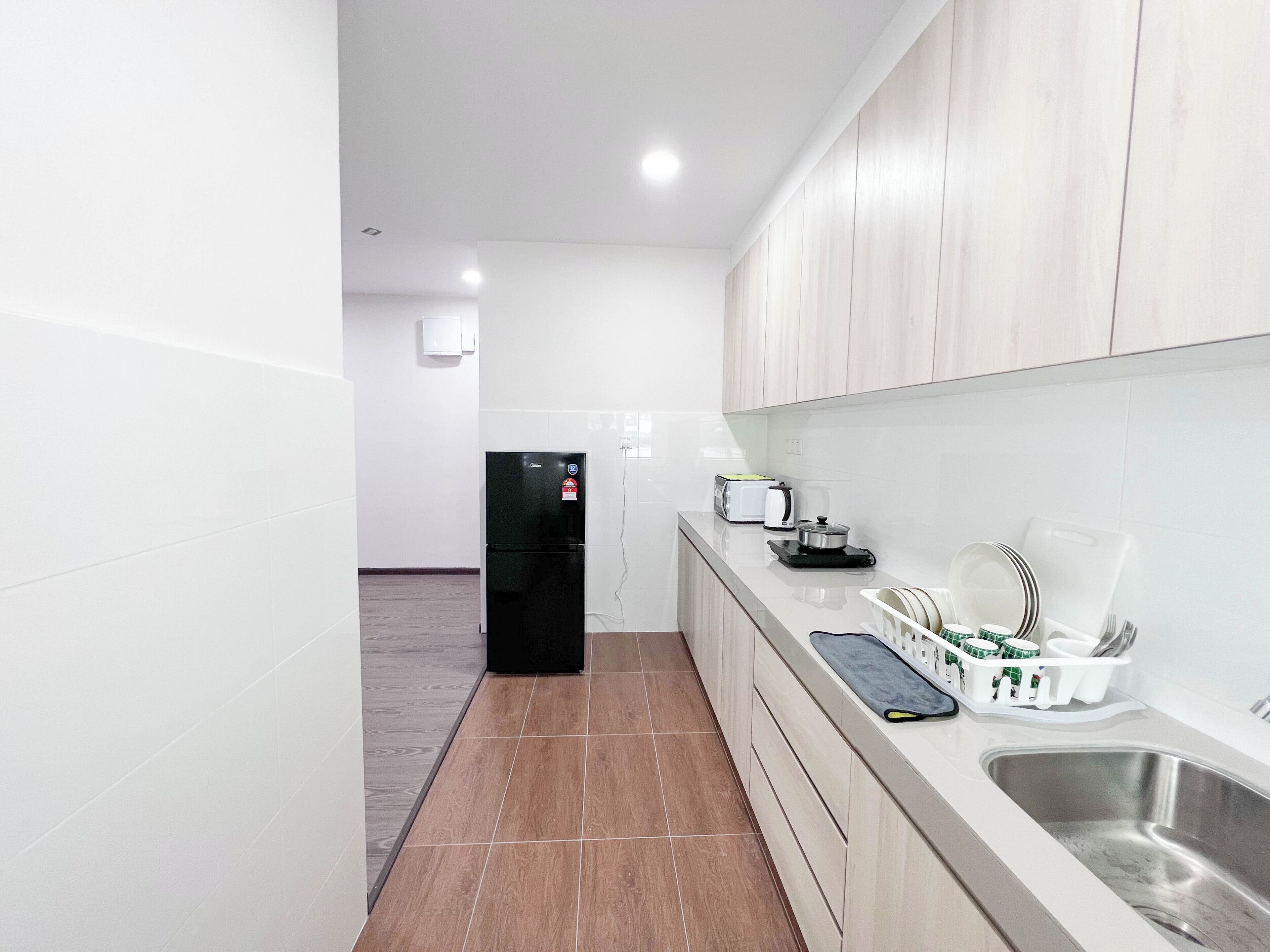 A modern kitchen with white cabinets, a black refrigerator, a stainless steel sink, and a countertop with a kettle and a toaster.