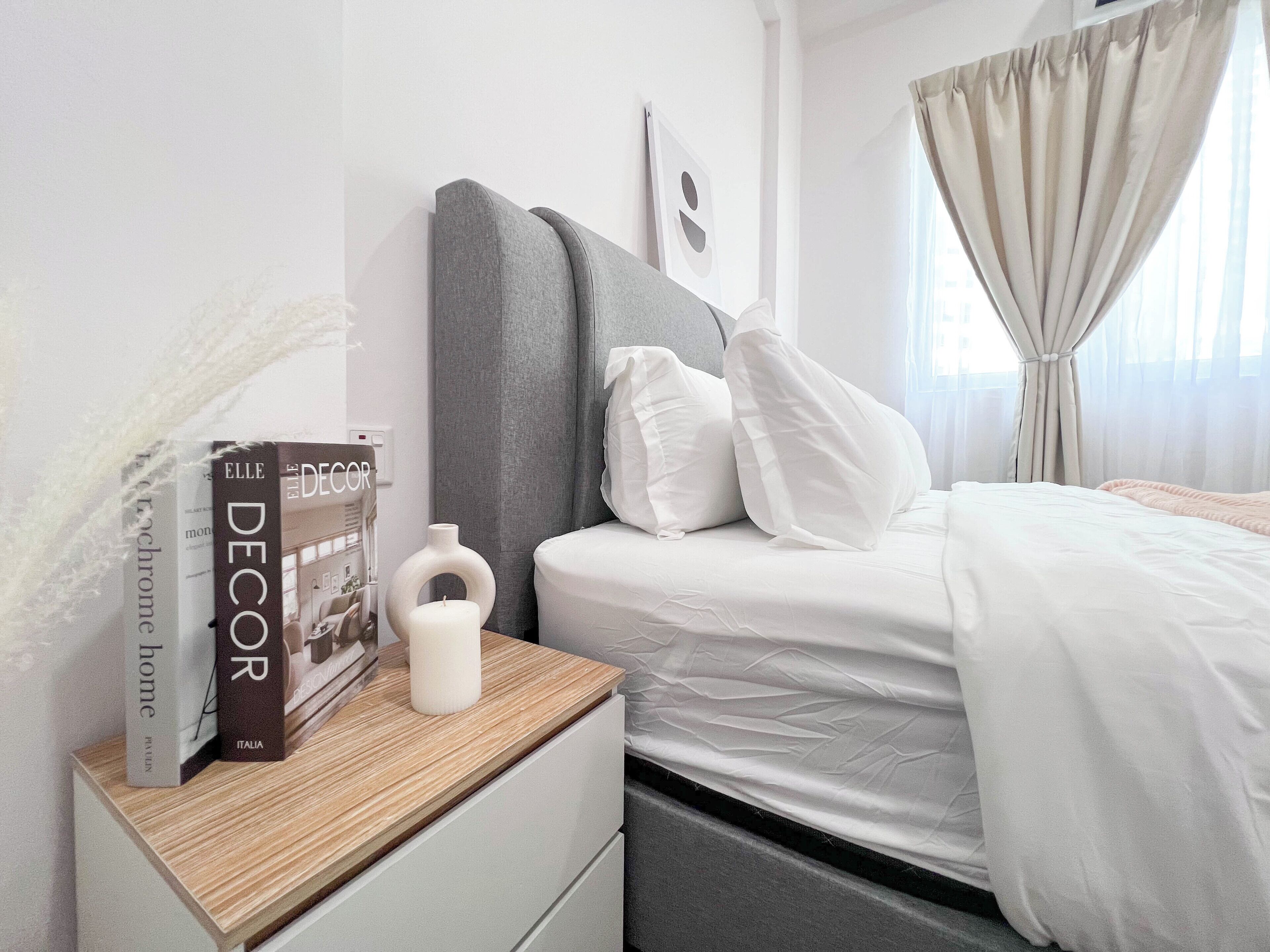 A neatly arranged hotel room with a bed, bedside table, and a book titled "ELLE DECOR".